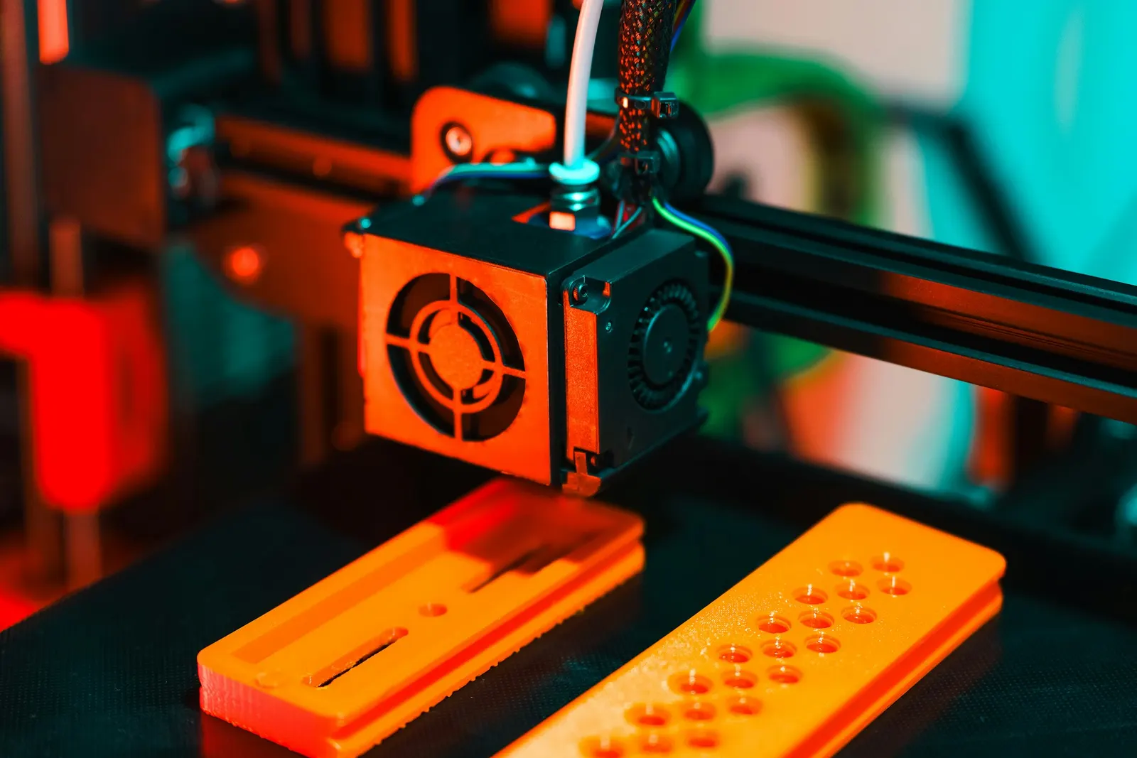 Close-up of a 3D printer nozzle laying down orange filament on a part