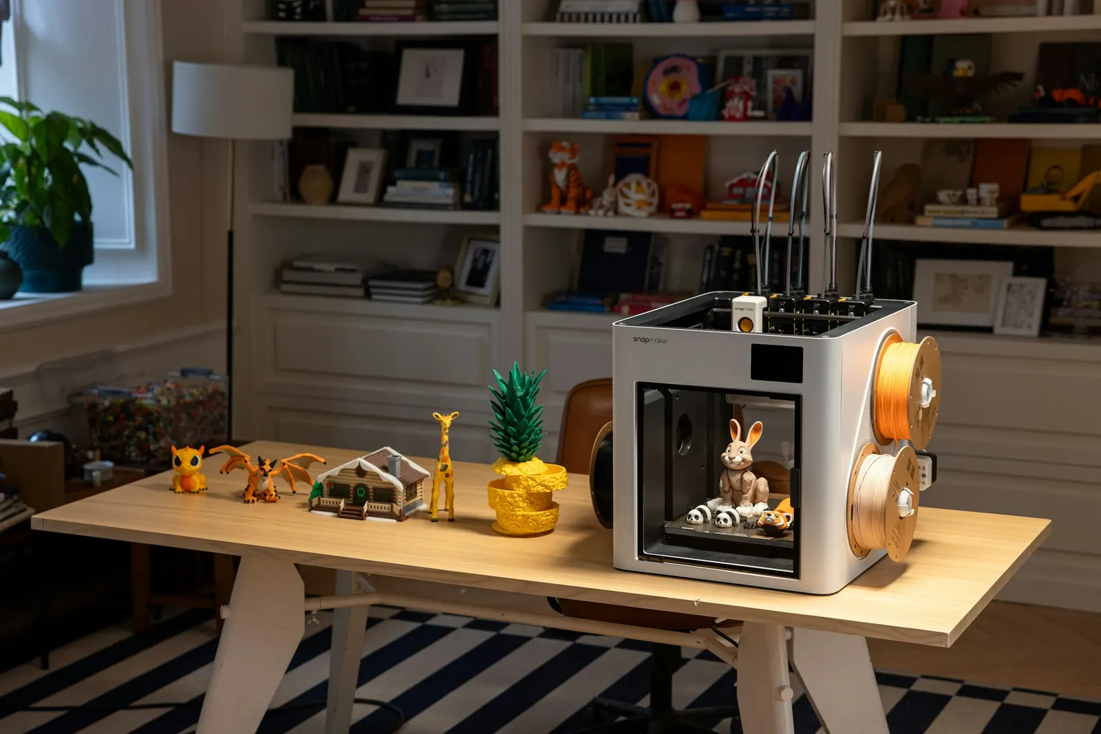 Desktop 3D printer surrounded by filament spools and colorful printed objects