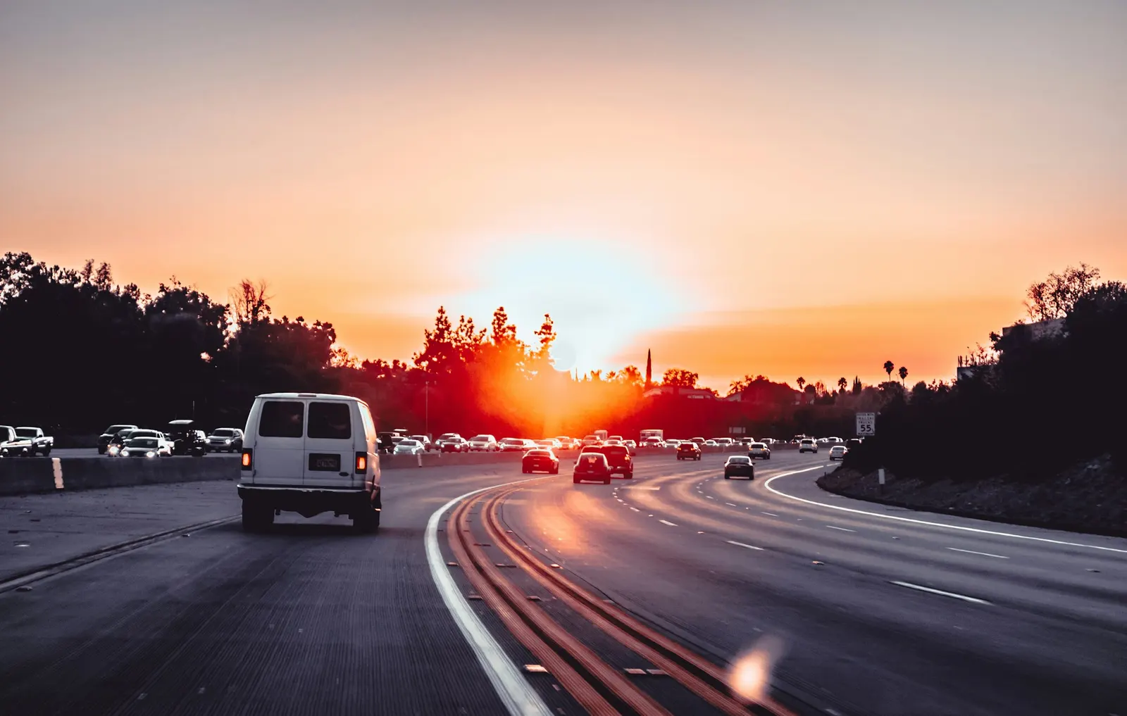 White cargo van cruising down a highway toward a golden sunrise