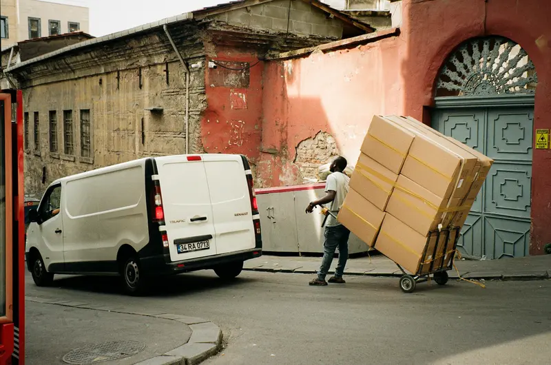 Courier wheeling stacked boxes from a white cargo van on a city street