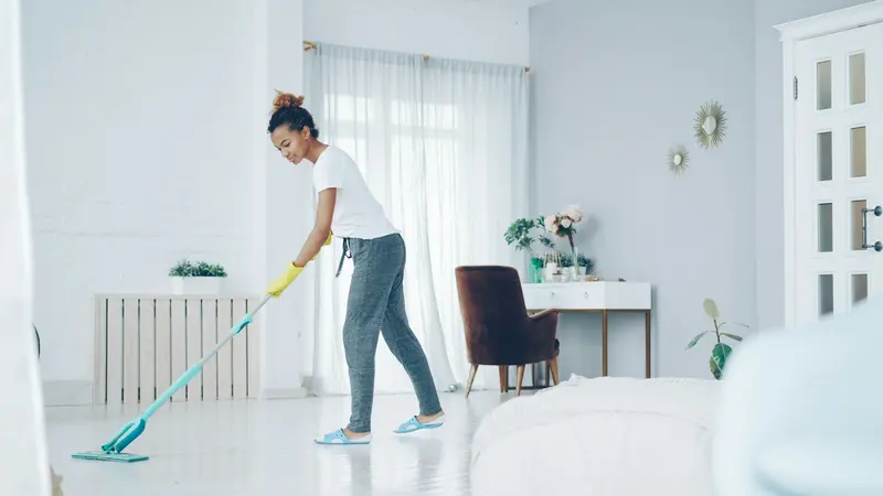Professional cleaner mopping the floor of a bright, modern bedroom