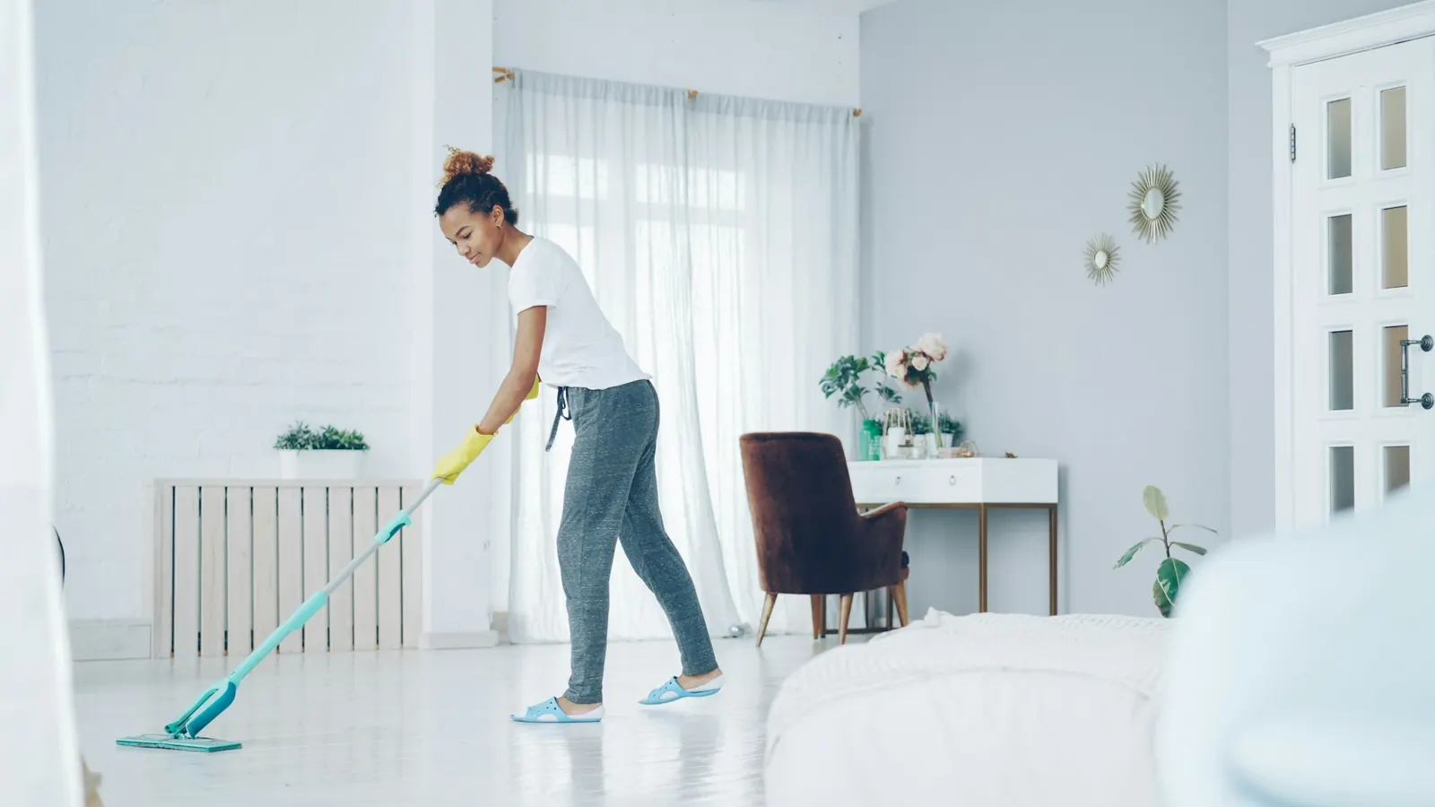 Professional cleaner mopping the floor of a bright, modern bedroom