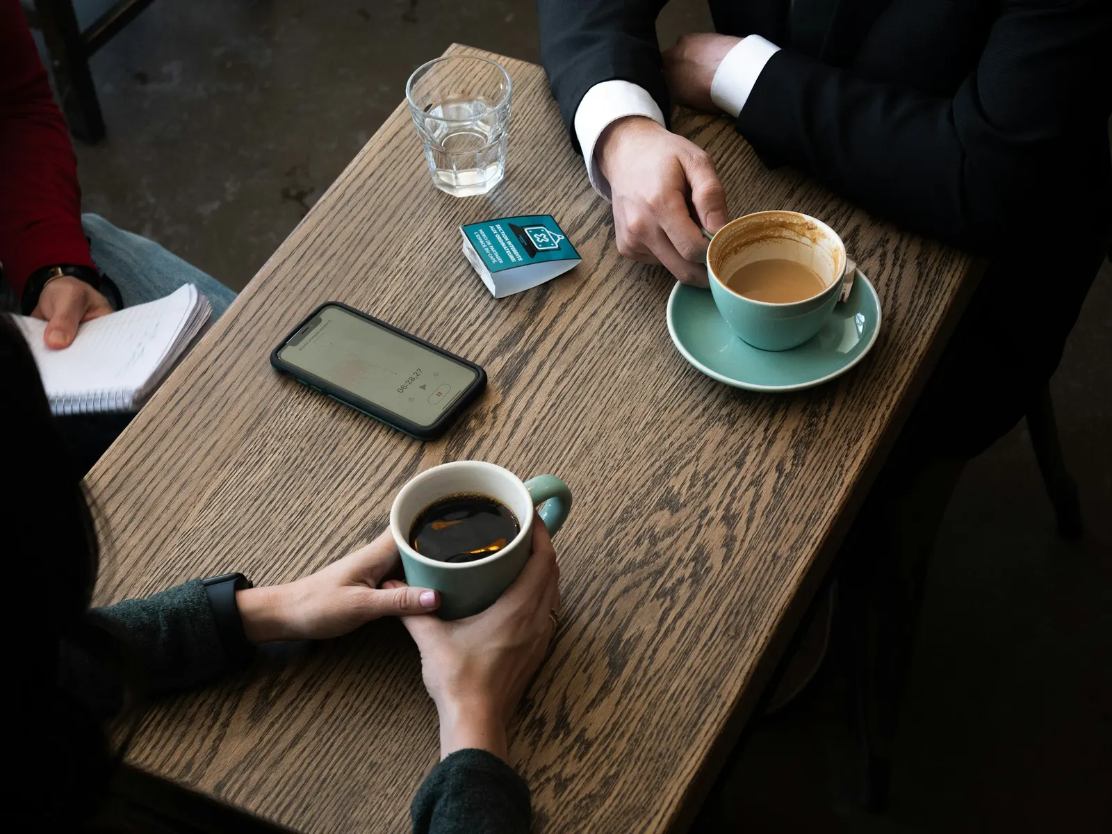 Two professionals talking over coffee with a notebook and phone on a wooden table