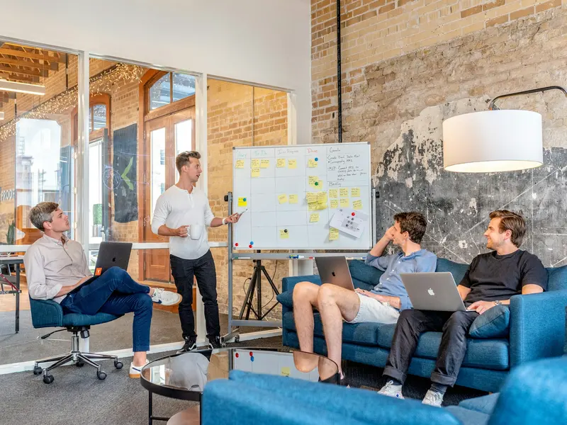 Consultant presenting a plan on a whiteboard to three colleagues in a loft meeting room