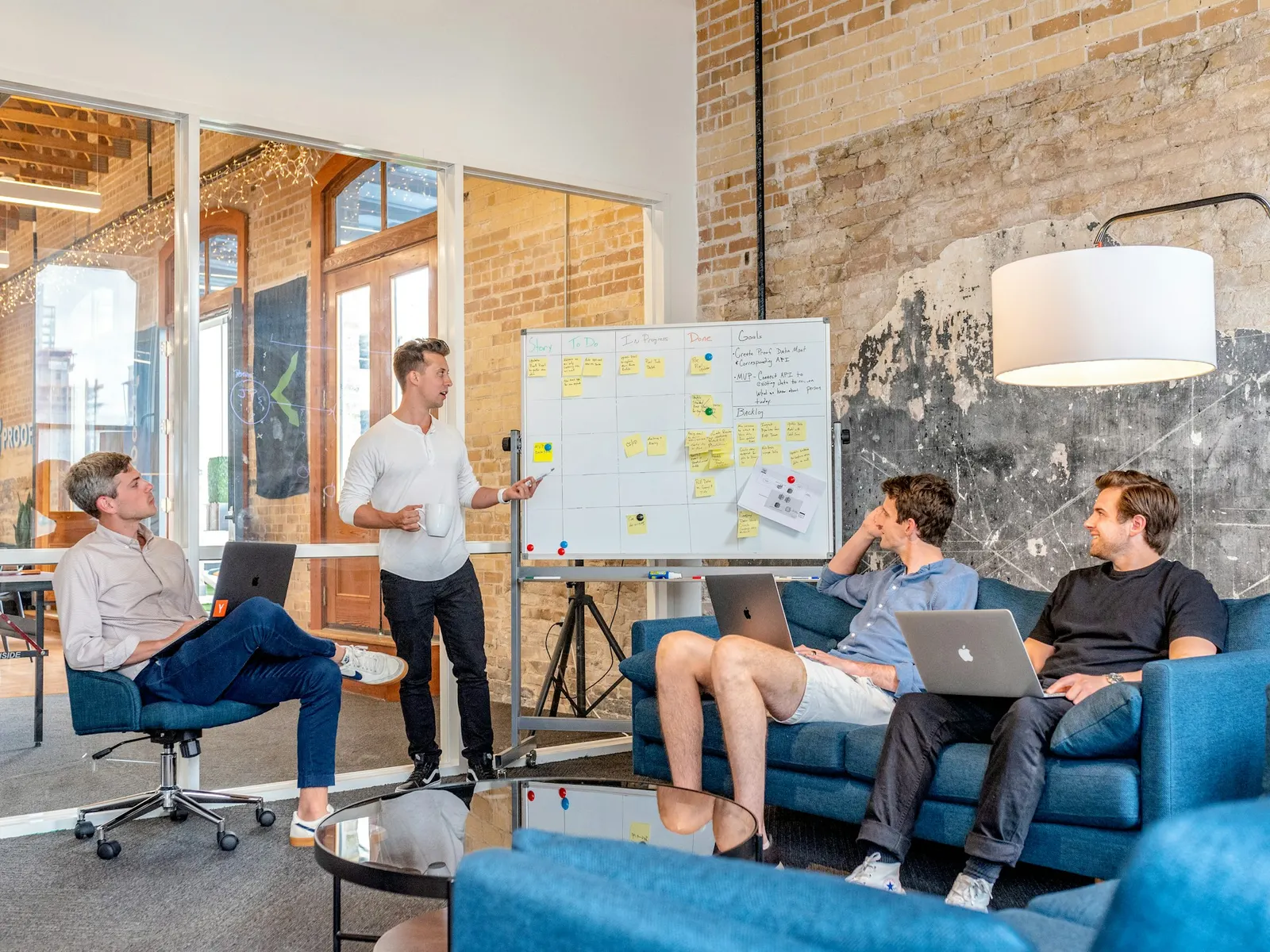 Consultant presenting a plan on a whiteboard to three colleagues in a loft meeting room