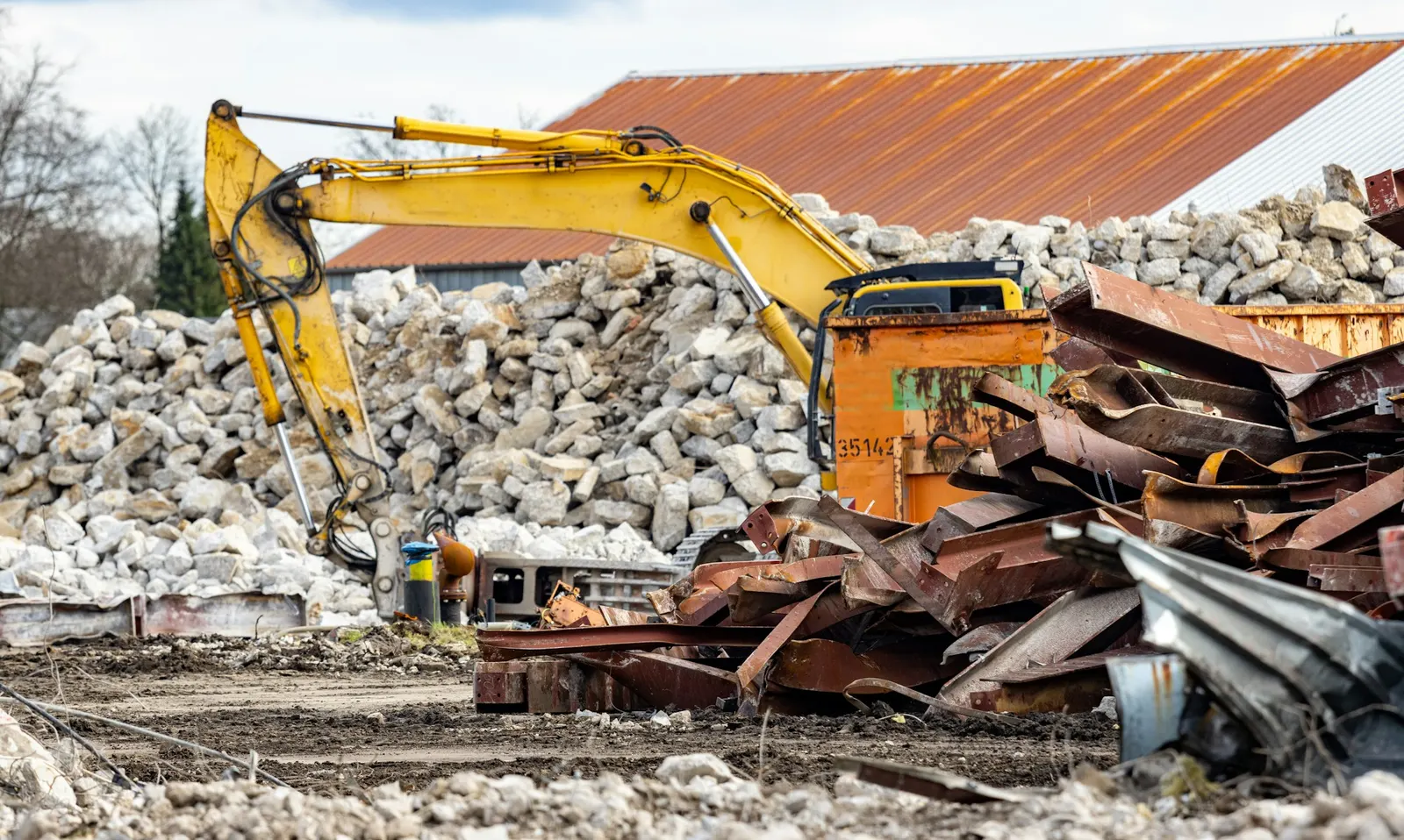 Pile of demolition rubble next to a yellow excavator on a job site