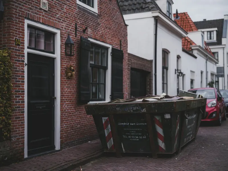 Rented skip dumpster loaded with renovation debris parked outside a brick townhouse