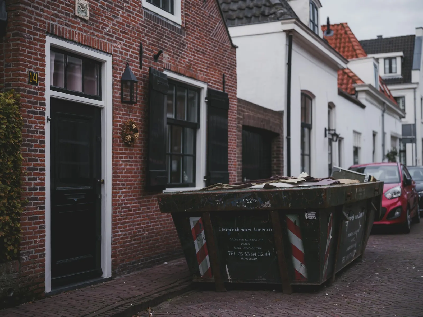 Rented skip dumpster loaded with renovation debris parked outside a brick townhouse