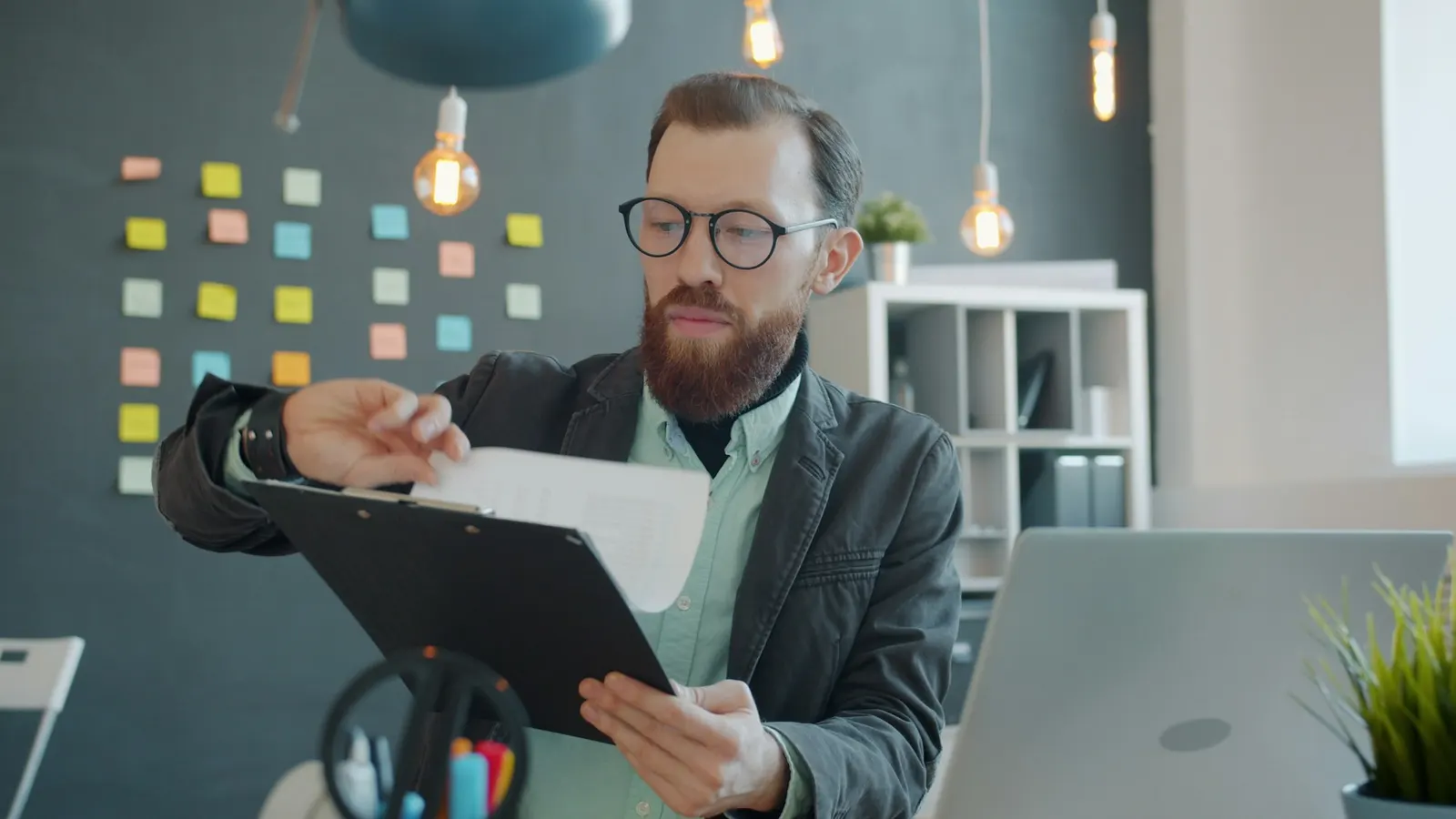 Editor in glasses reviewing a printed document on a clipboard at his desk