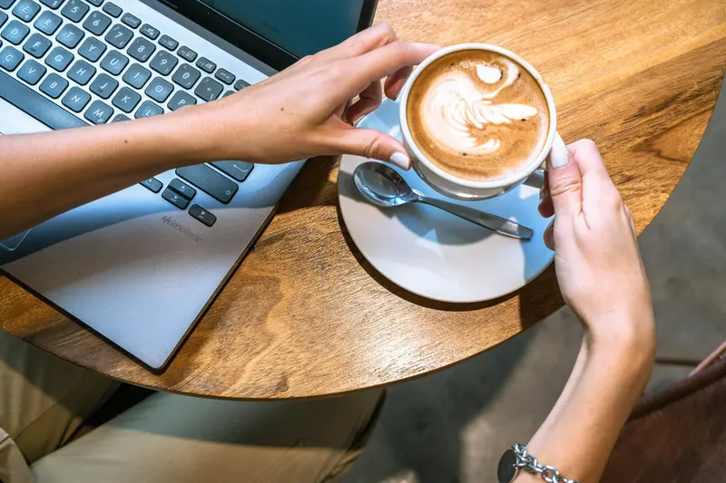 Writer working on a laptop at a sunny cafe table with a fresh latte
