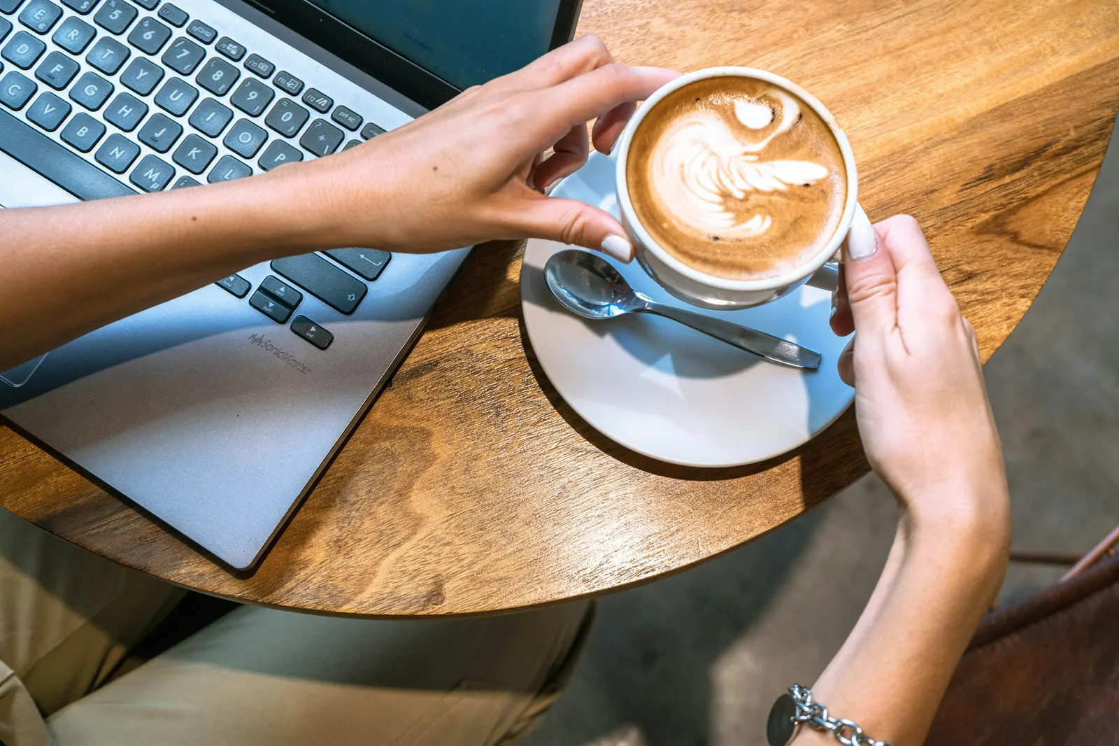Writer working on a laptop at a sunny cafe table with a fresh latte