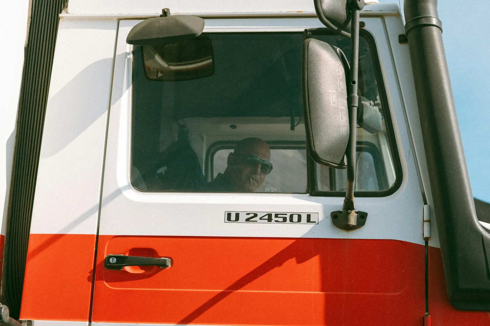 Truck driver seen through the cab window beside a large side mirror