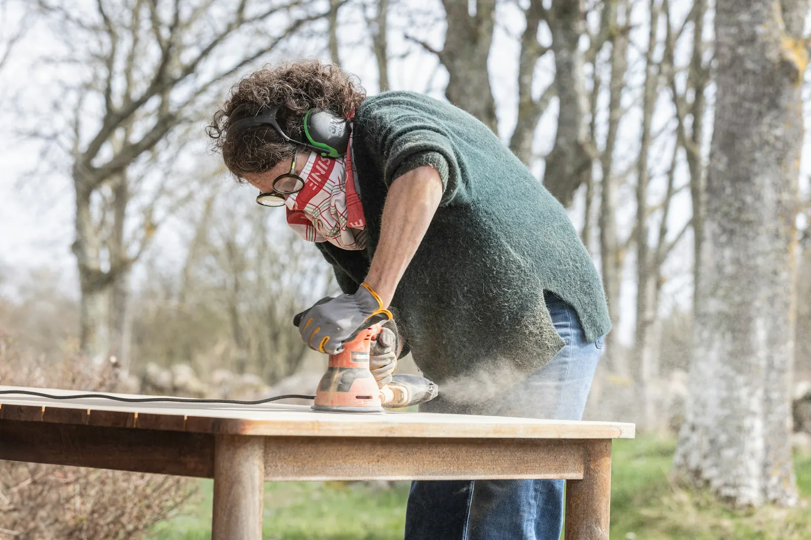 Woman sanding a wooden table top with an orbital sander outdoors
