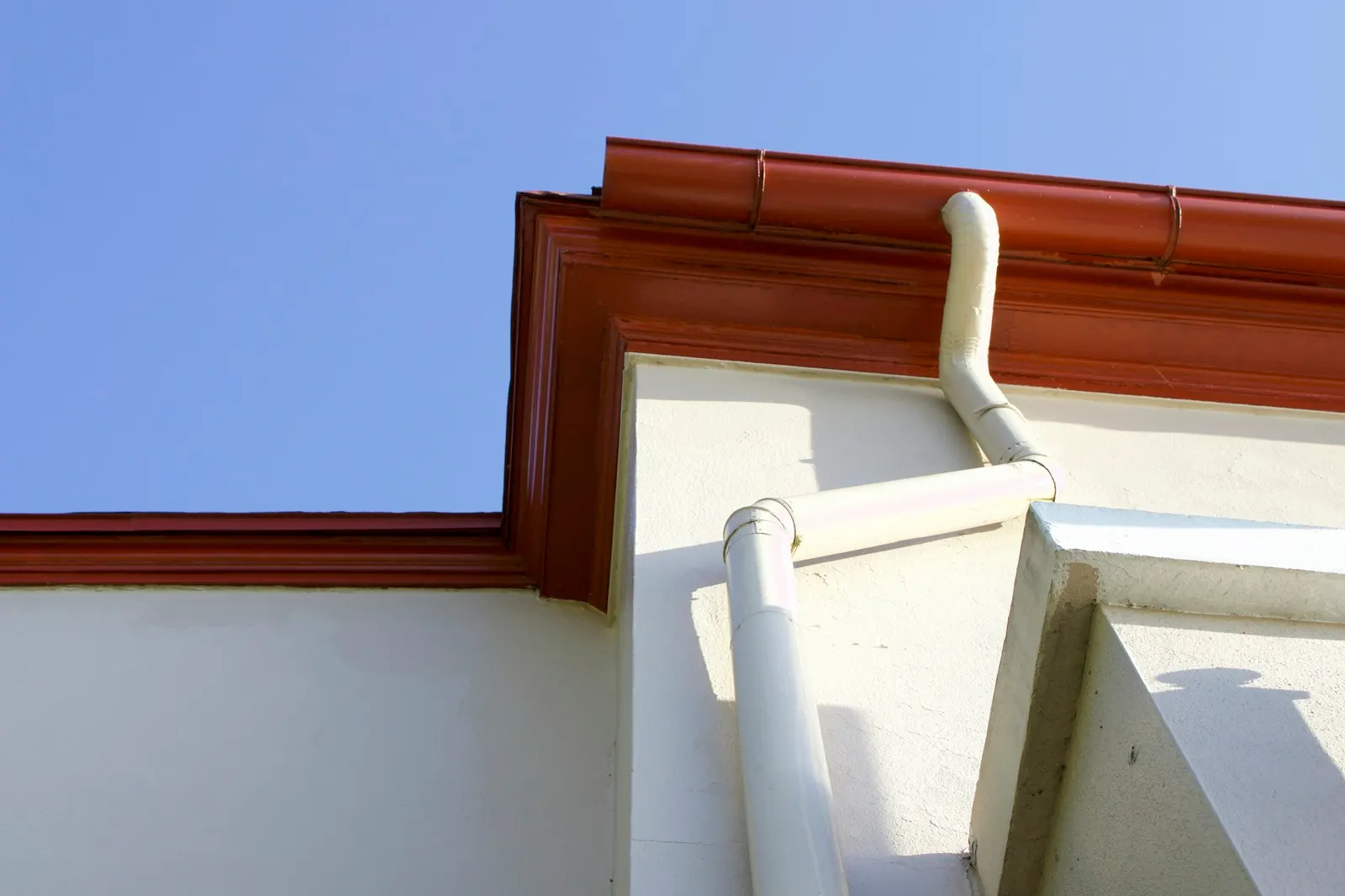 Clean white gutter and downspout on the corner of a suburban house