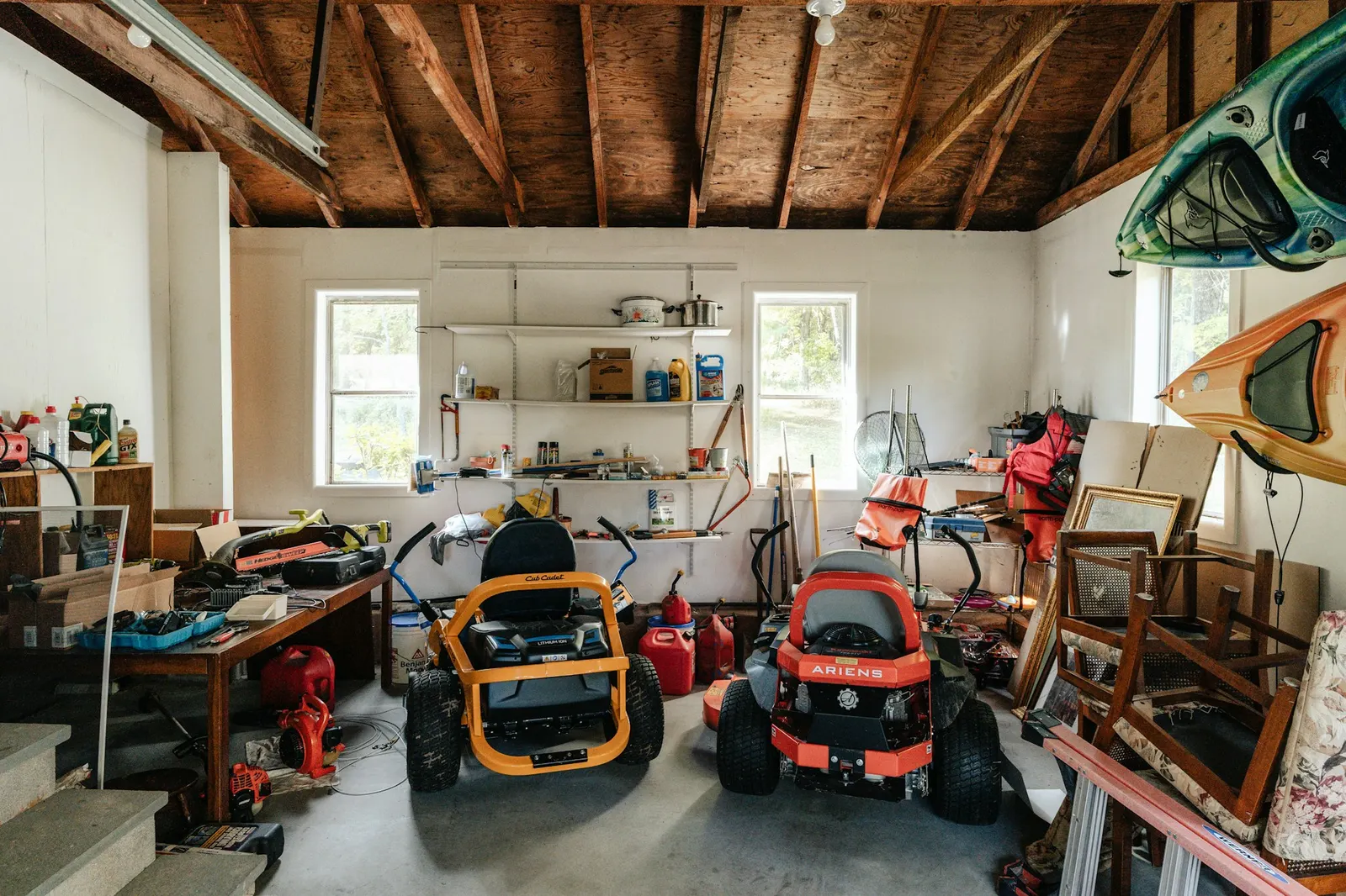 Cluttered garage packed with mowers, tools, frames and old household items