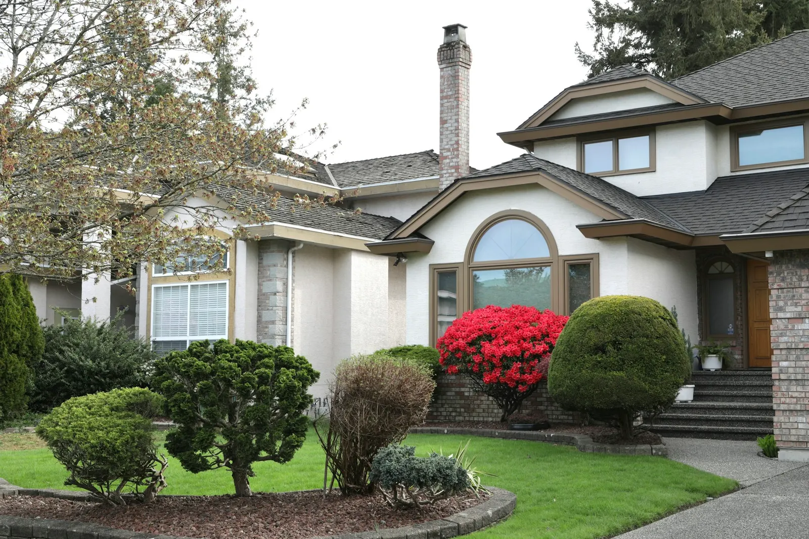 Large house with manicured shrubs, red flowers, and a tidy front yard