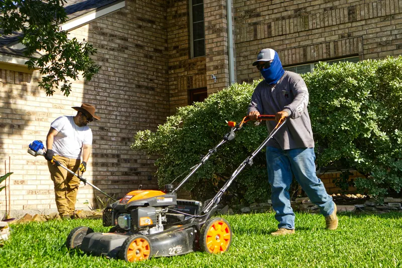 Two lawn care workers mowing and trimming a lush residential lawn