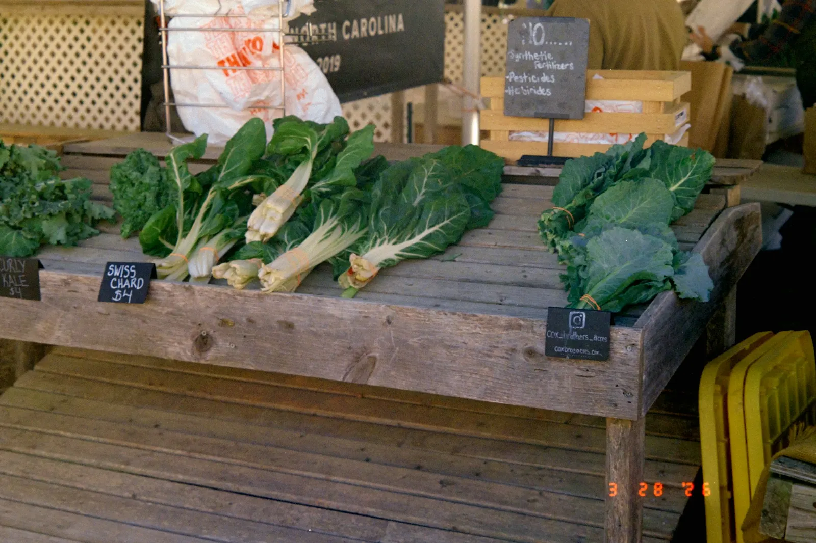 Fresh leafy greens displayed for sale on a wooden farmers market stall