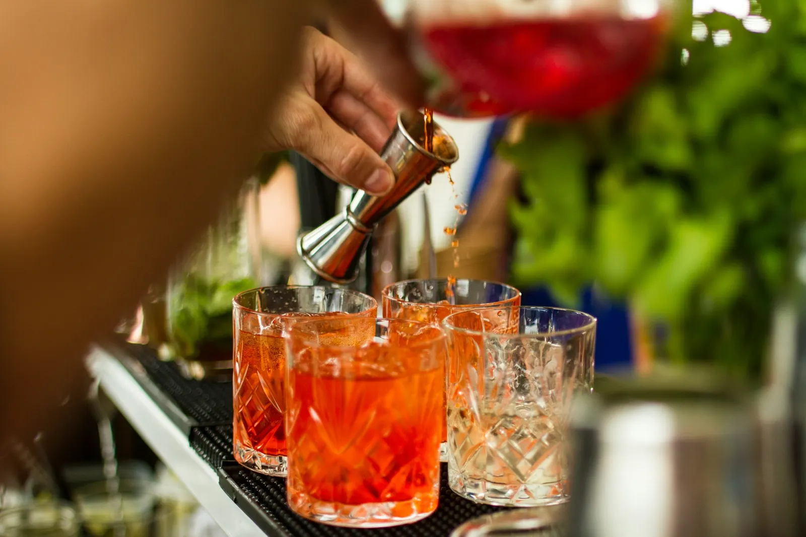 Bartender pouring drinks into a row of glasses lined up on an event bar
