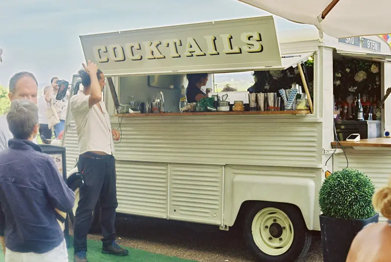 Bartender serving cocktails from a cream vintage van converted into a mobile bar