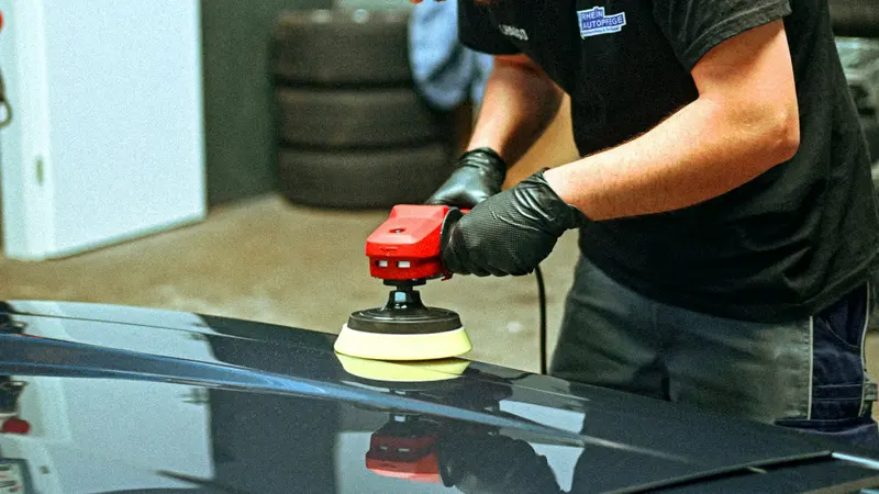 Detailer polishing a dark car's paintwork with an electric buffer