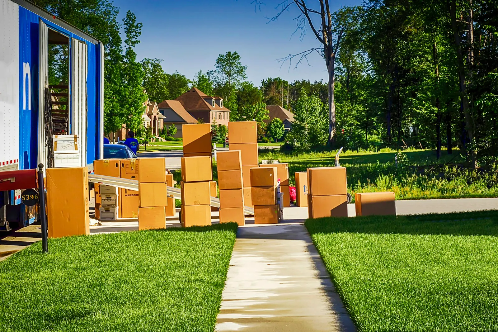 Moving truck parked on a sunny lawn beside stacks of cardboard boxes