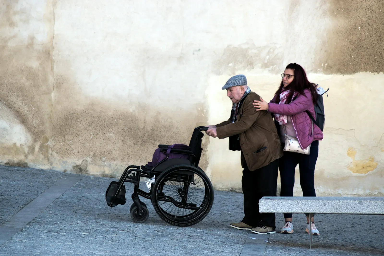 Caregiver steadying an elderly man as he stands up from his wheelchair outdoors