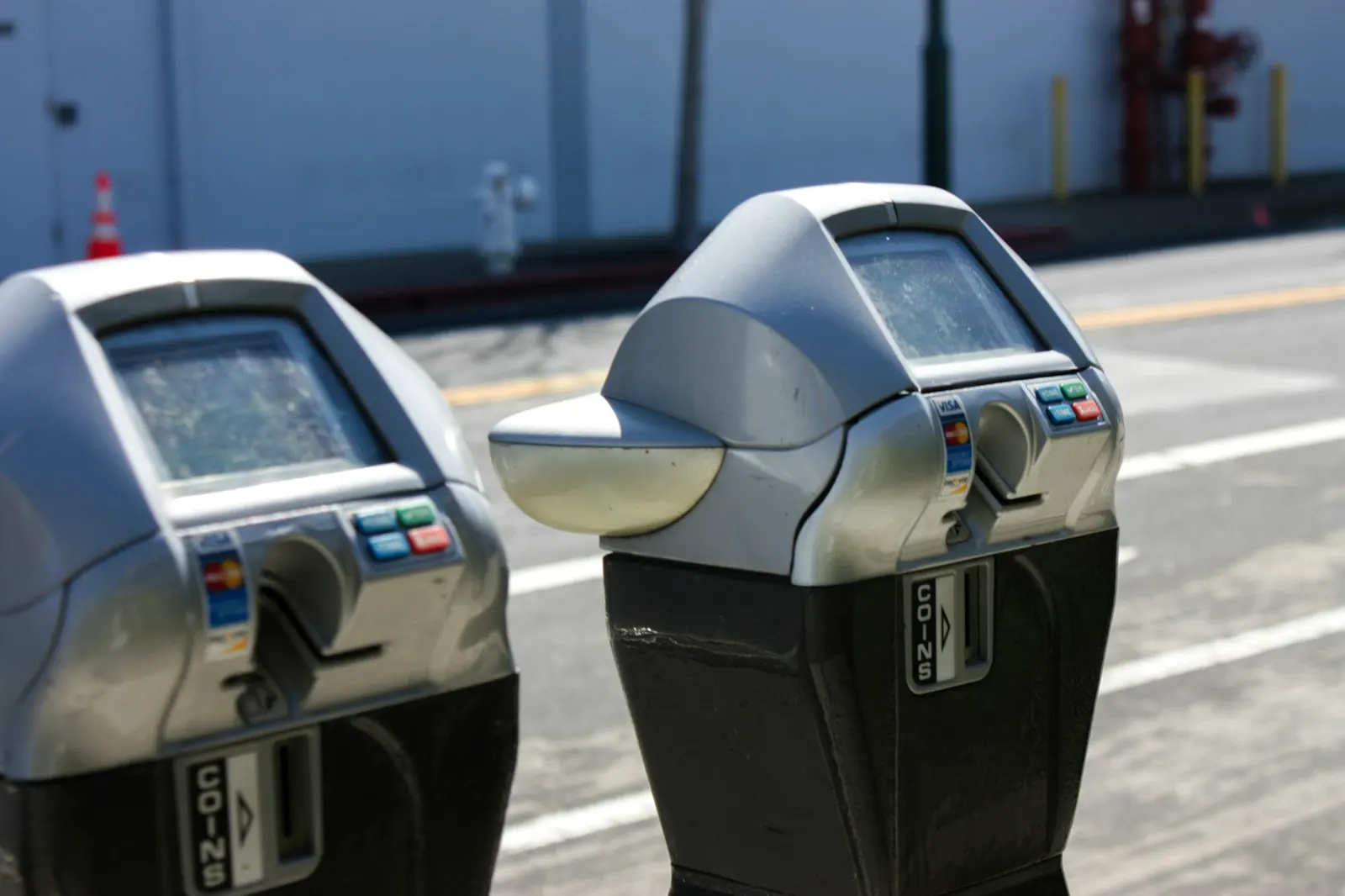 Two modern card-reader parking meters beside marked spaces on a sunny street