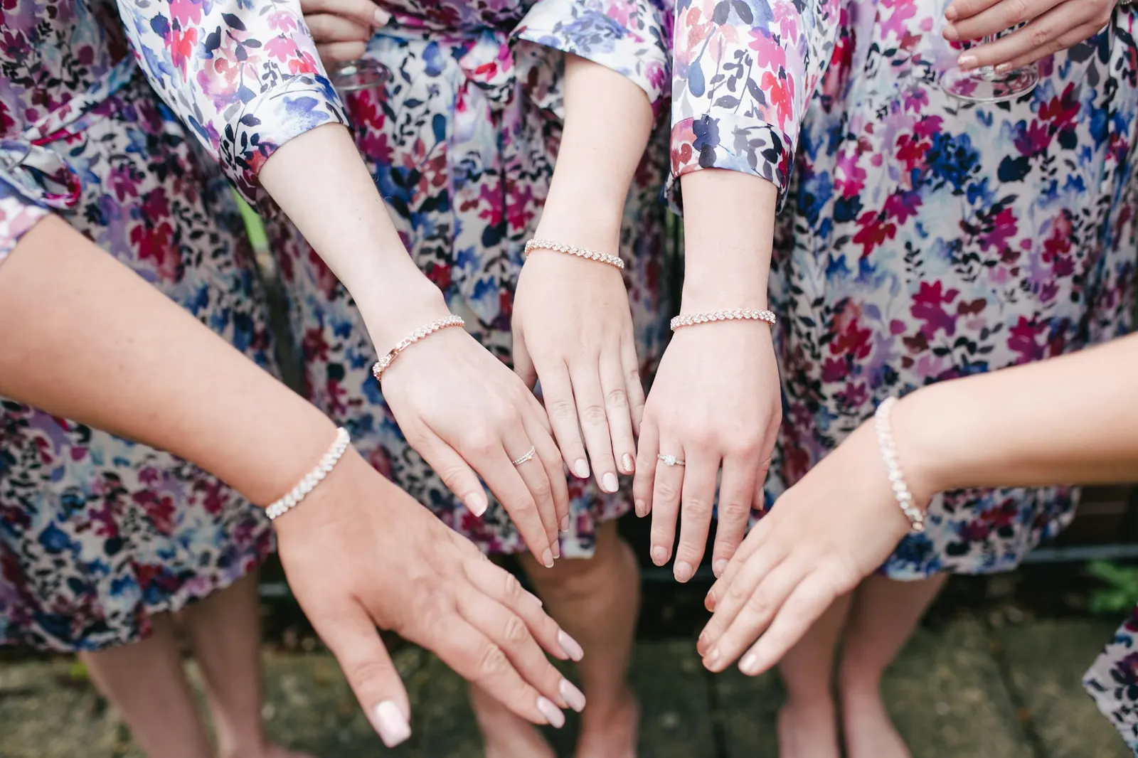 Four friends in floral dresses showing off matching bracelets on their wrists