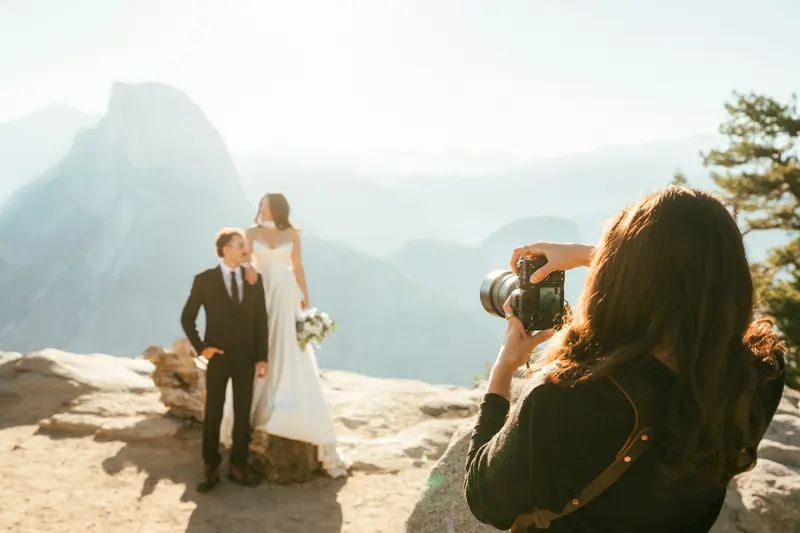 Photographer shooting a bride and groom on a mountain overlook at golden hour