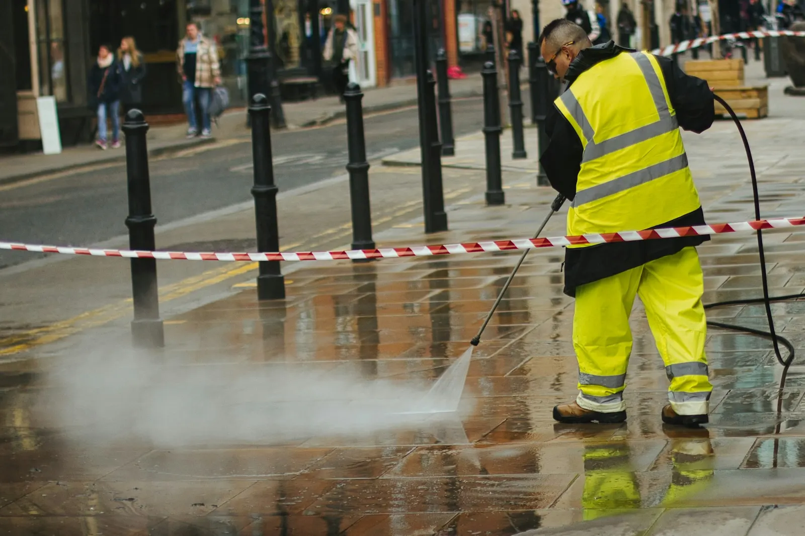 Worker in a hi-vis jacket pressure washing paving with a wand