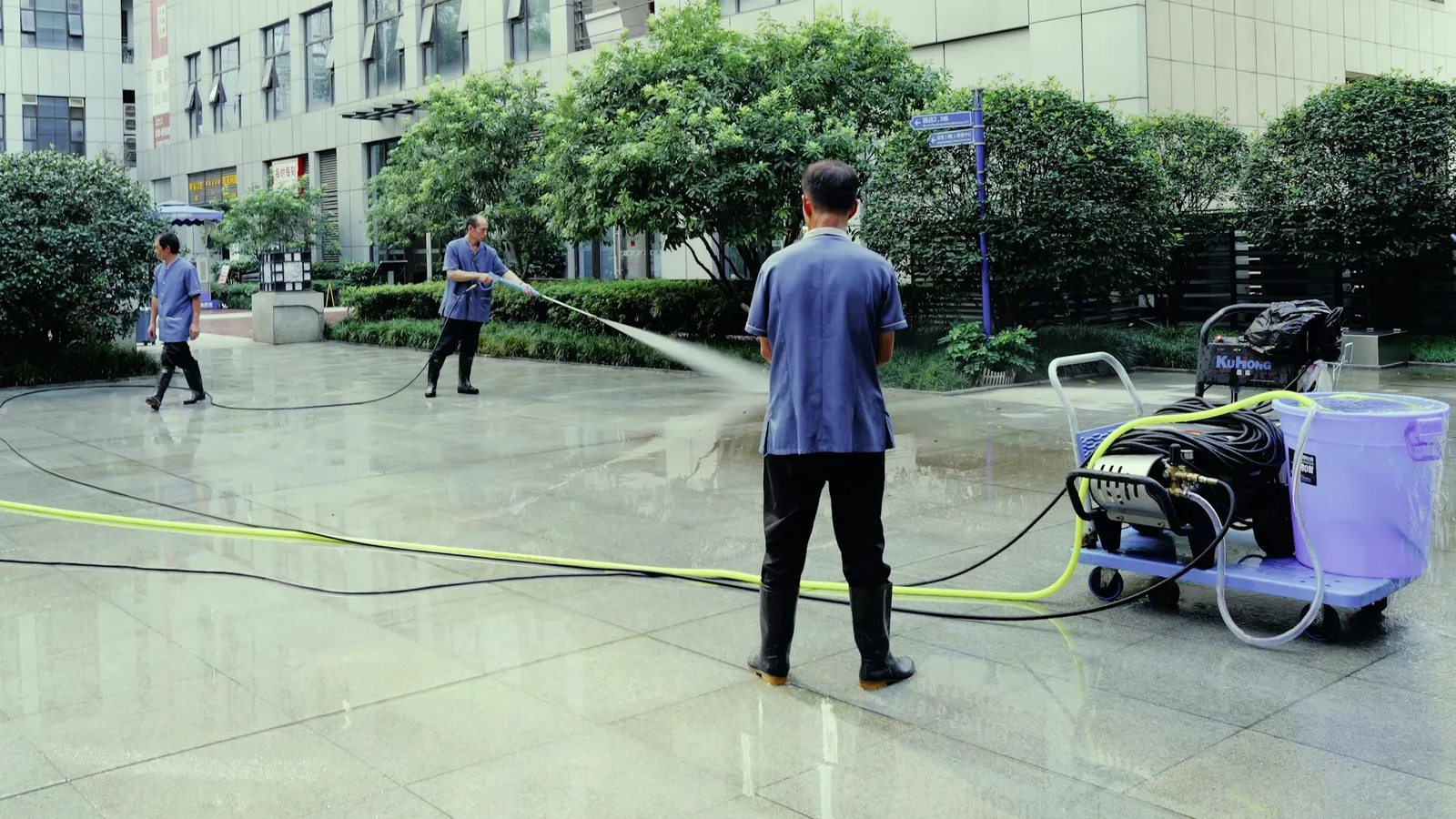 Worker pressure washing a wide concrete plaza with a wheeled power washer