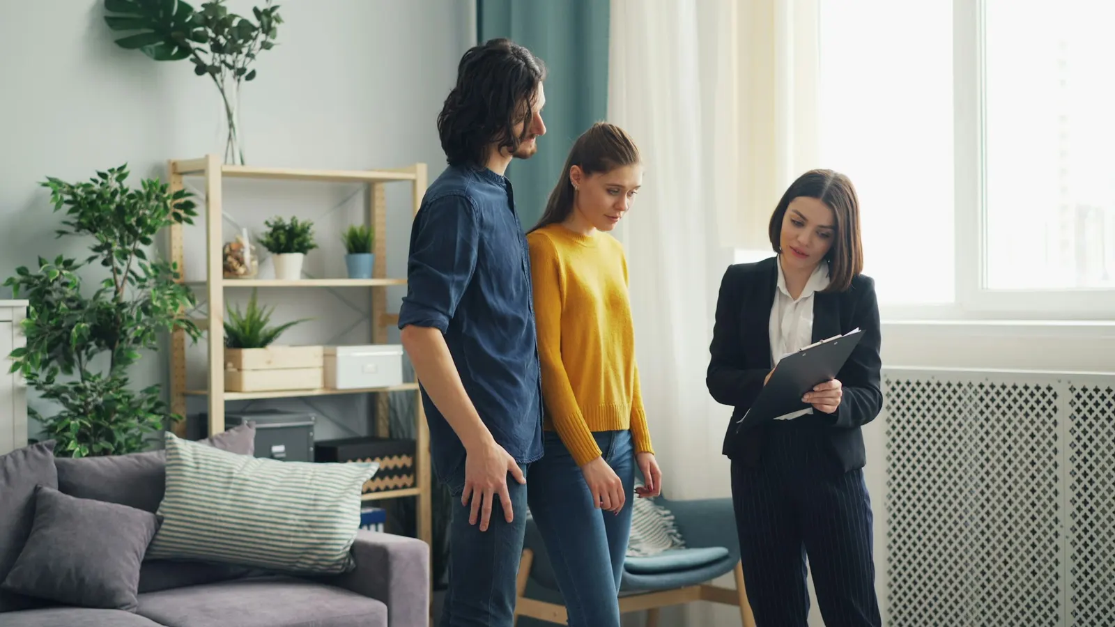Property manager with a clipboard walking a young couple through a furnished apartment