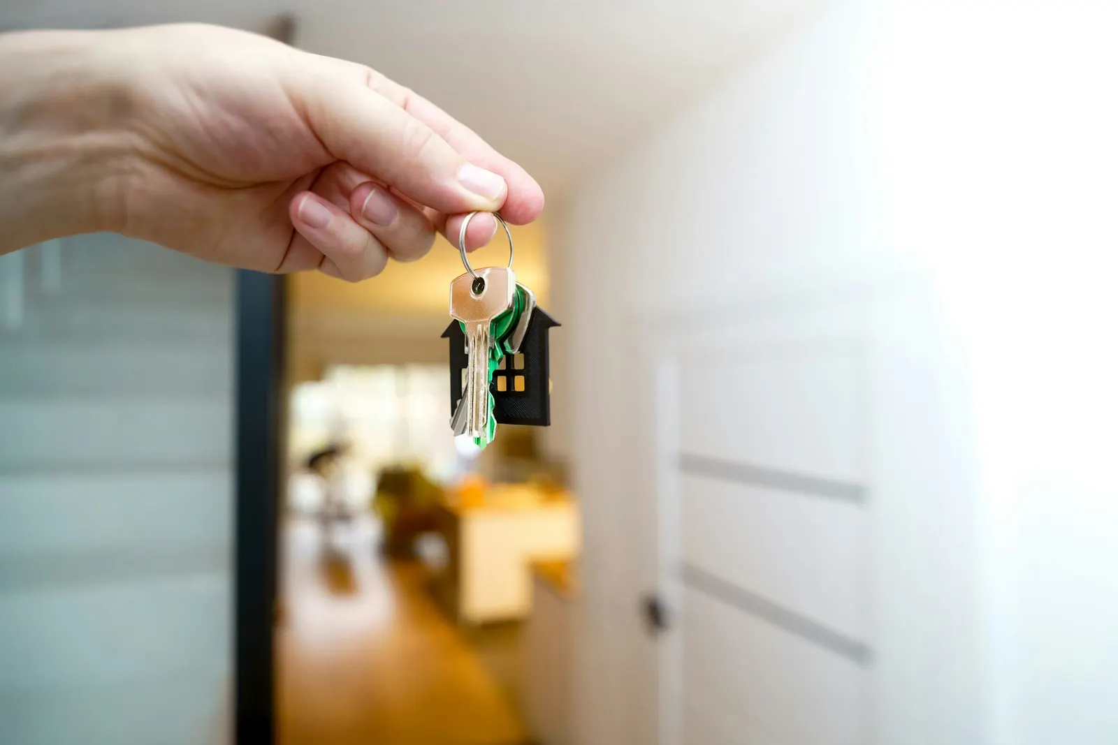 Hand holding house keys with a house-shaped keychain at the front entrance of a home