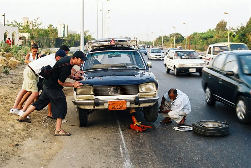 Man changing a flat tire on a car stopped at the side of a busy road