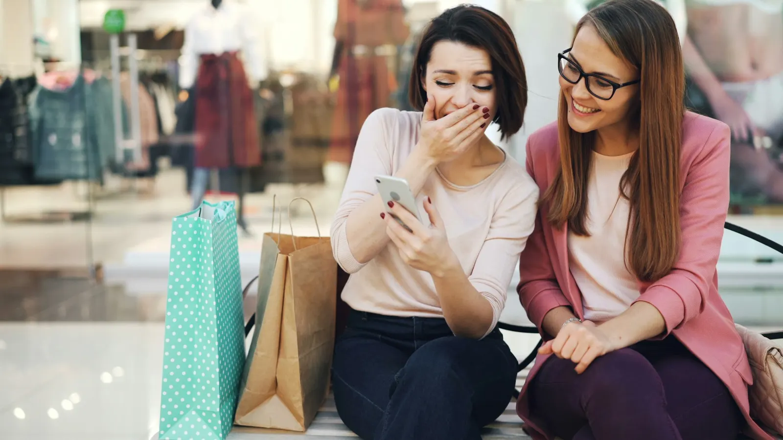 Two women laughing together while reviewing a post on a smartphone