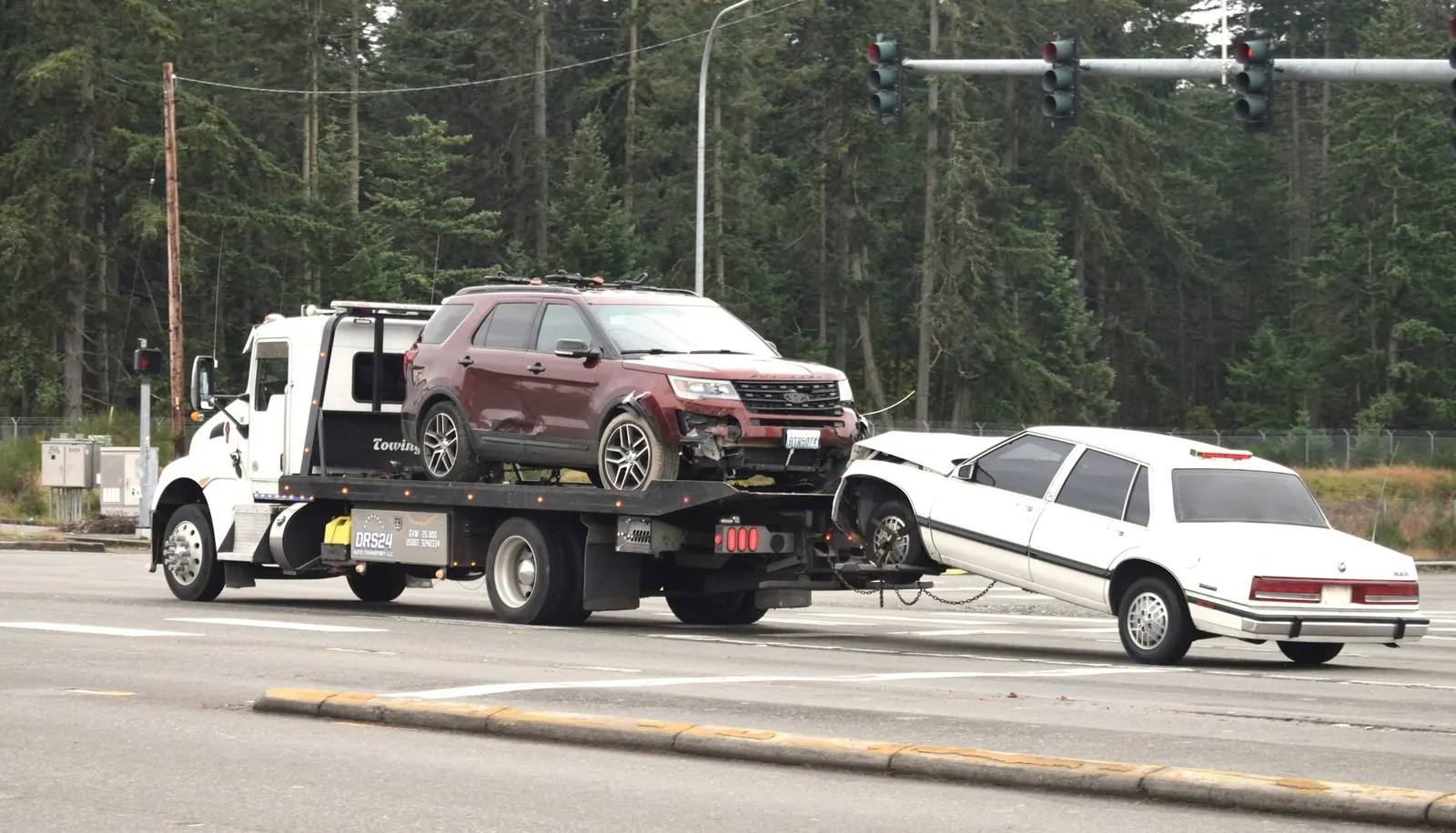 Wheel-lift tow truck hauling an SUV and a sedan through an intersection