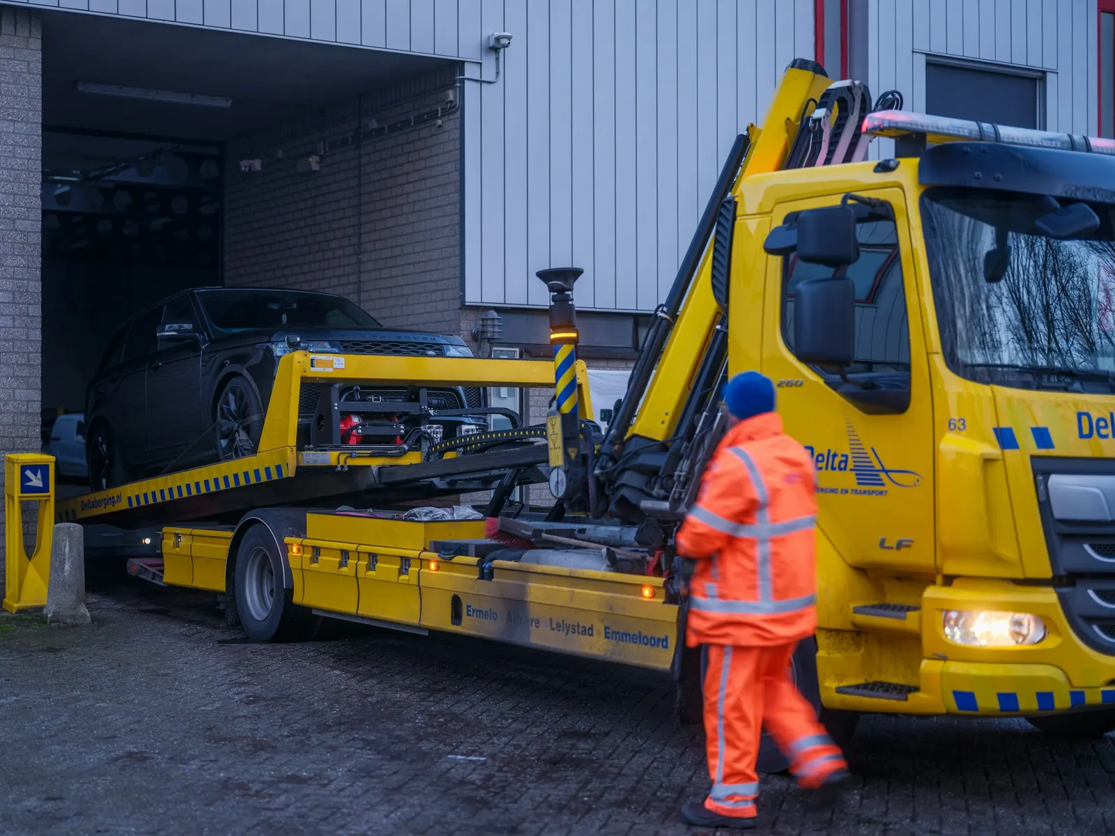 Operator in orange safety gear checking a car loaded on a yellow flatbed