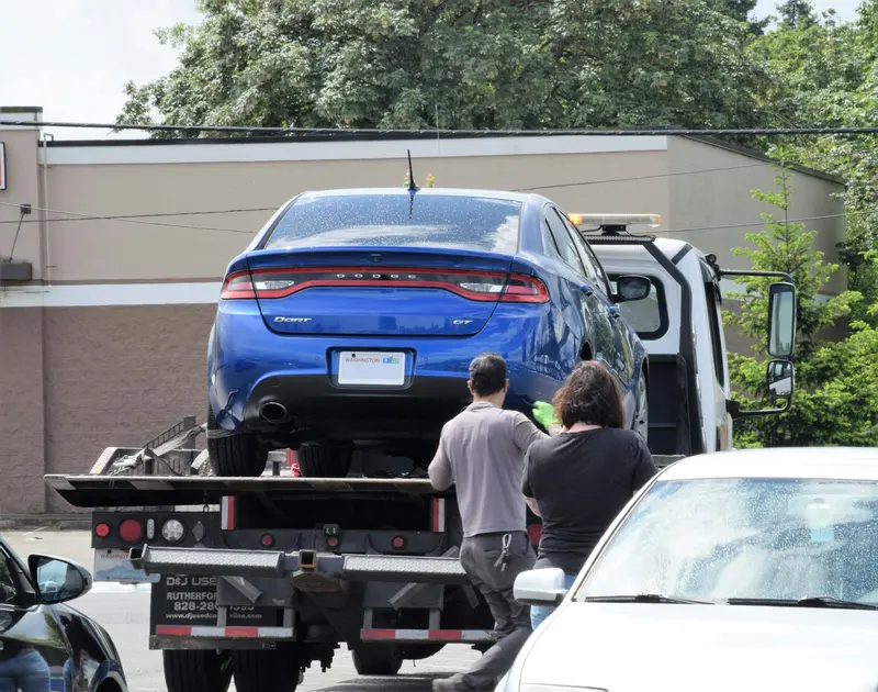 Operators securing a blue car on a flatbed tow truck at the roadside