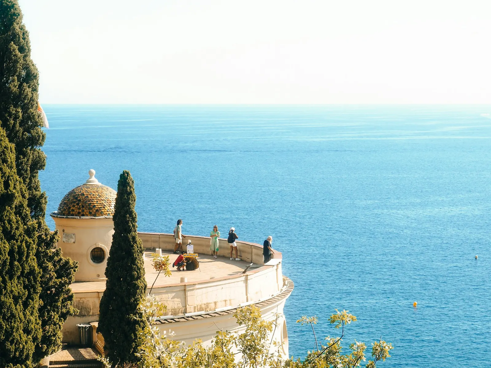 Travelers on a clifftop balcony overlooking the deep blue sea