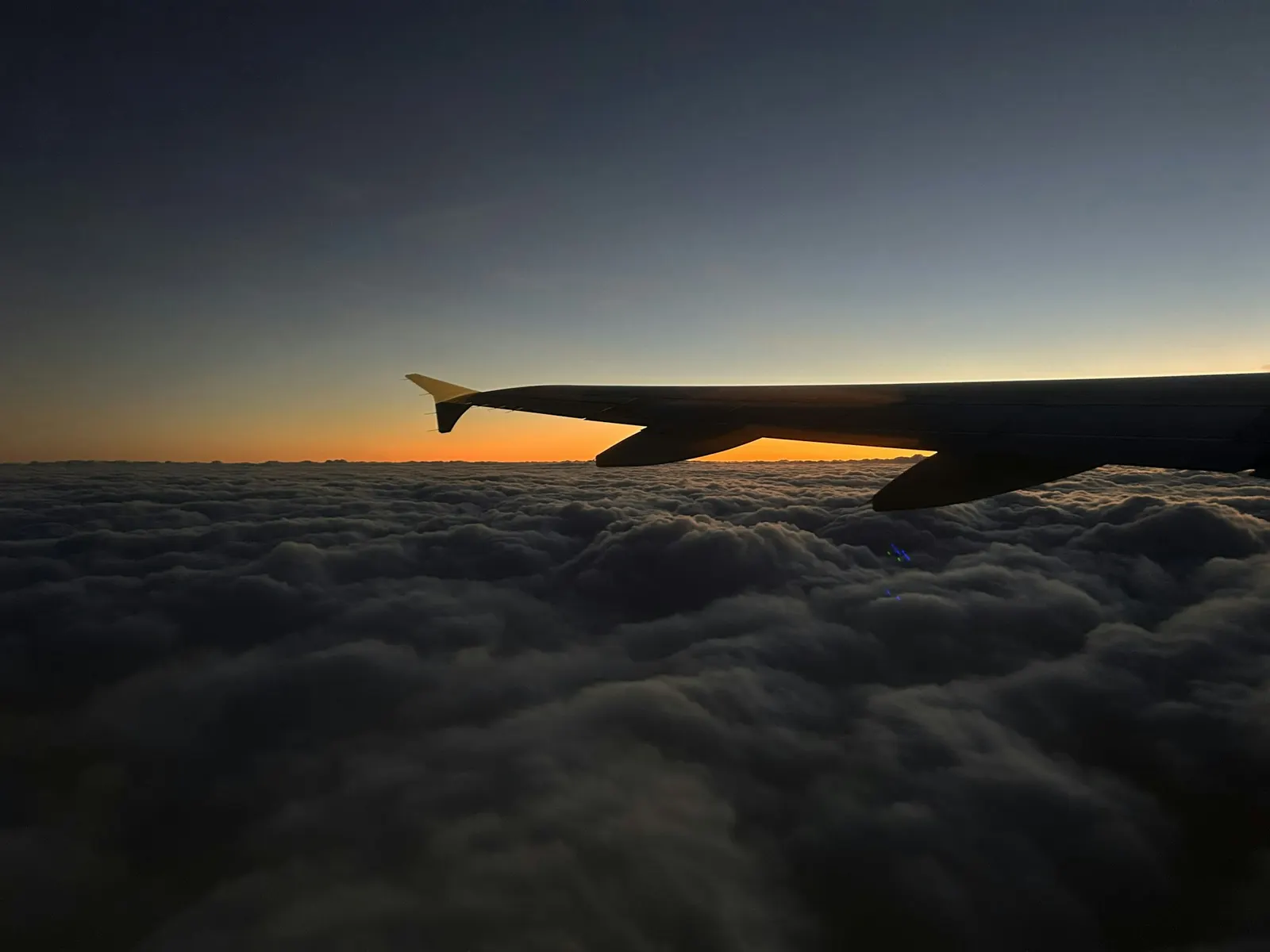 Airplane wing above a sea of clouds at sunset