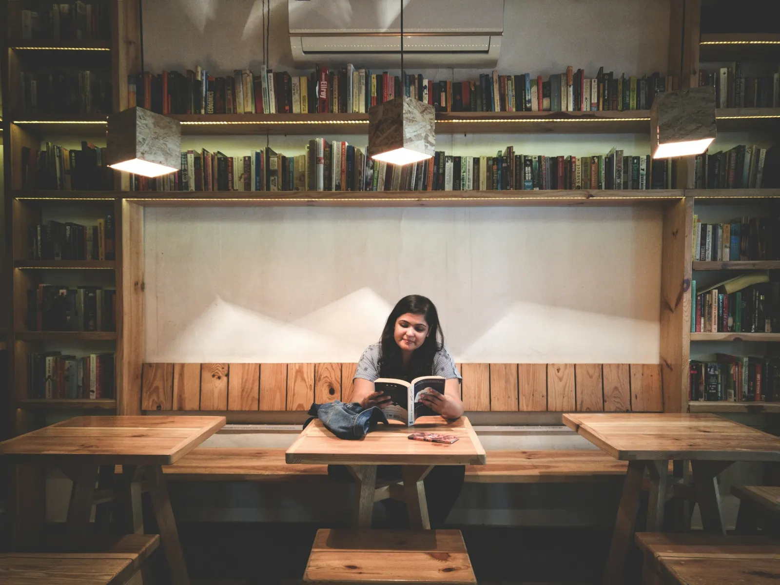 Smiling student reading a book at a table surrounded by library shelves
