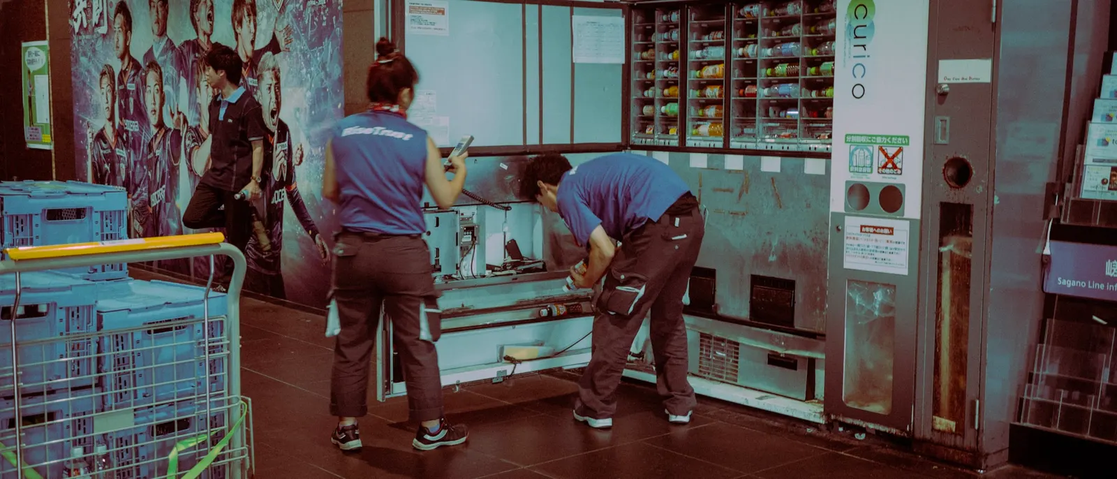 Two uniformed workers servicing and restocking an open vending machine