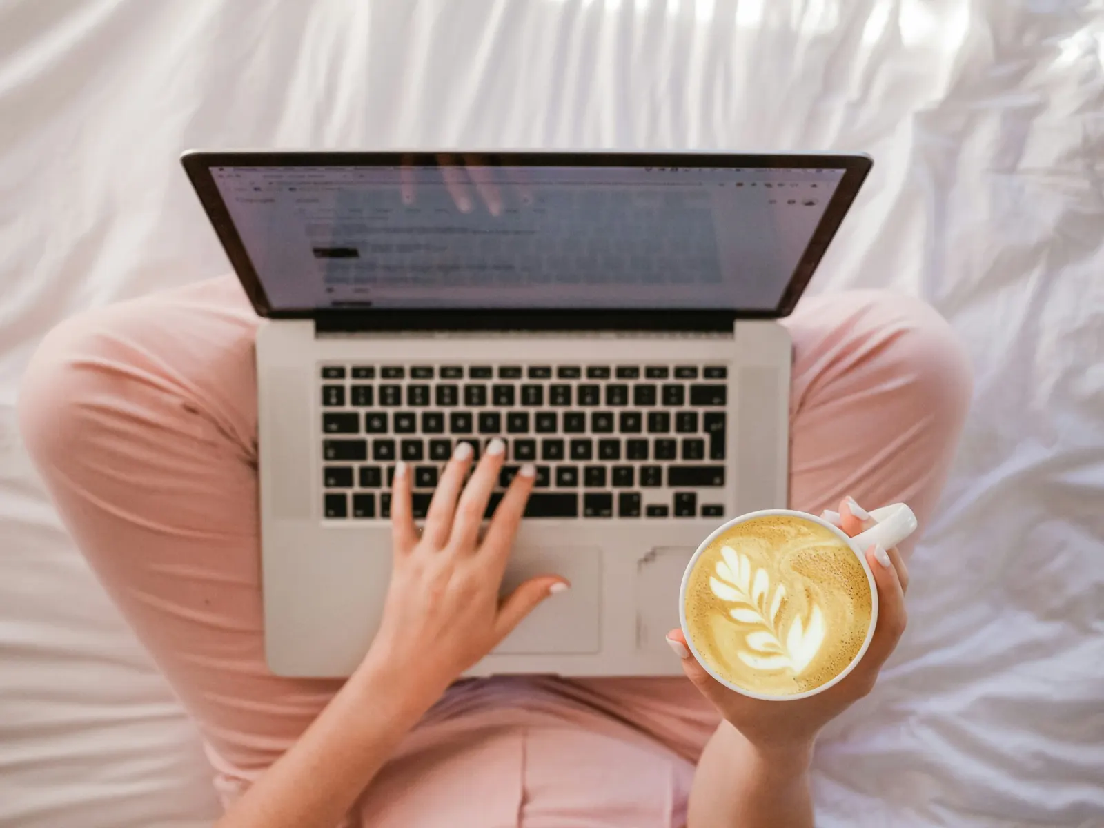 Working through messages on a laptop while holding a cappuccino