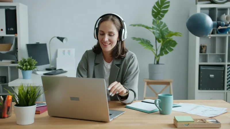 Smiling virtual assistant wearing a headset working on a laptop in a tidy home office