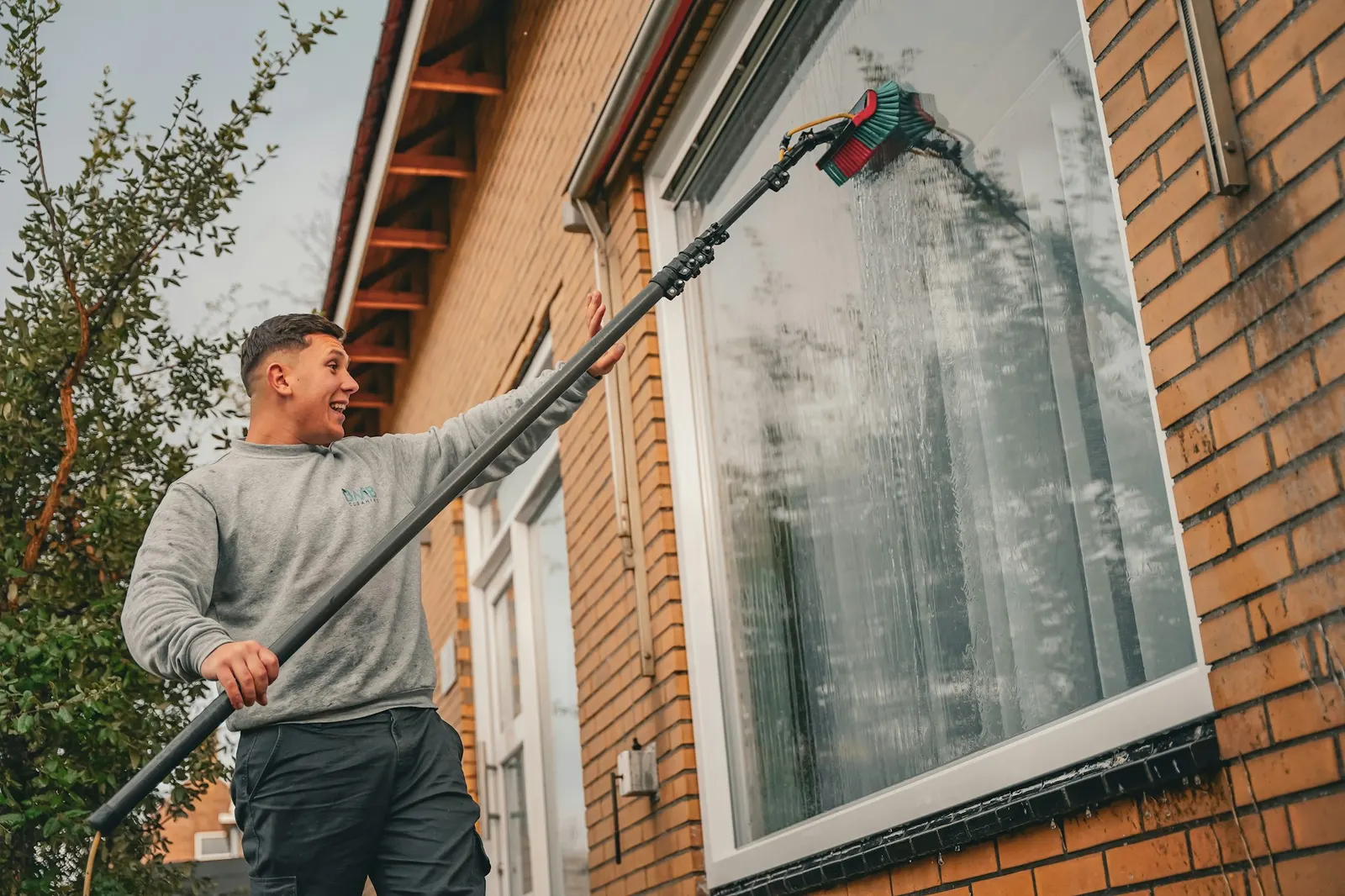 Window cleaner using a tall extension pole to reach upper windows of a house