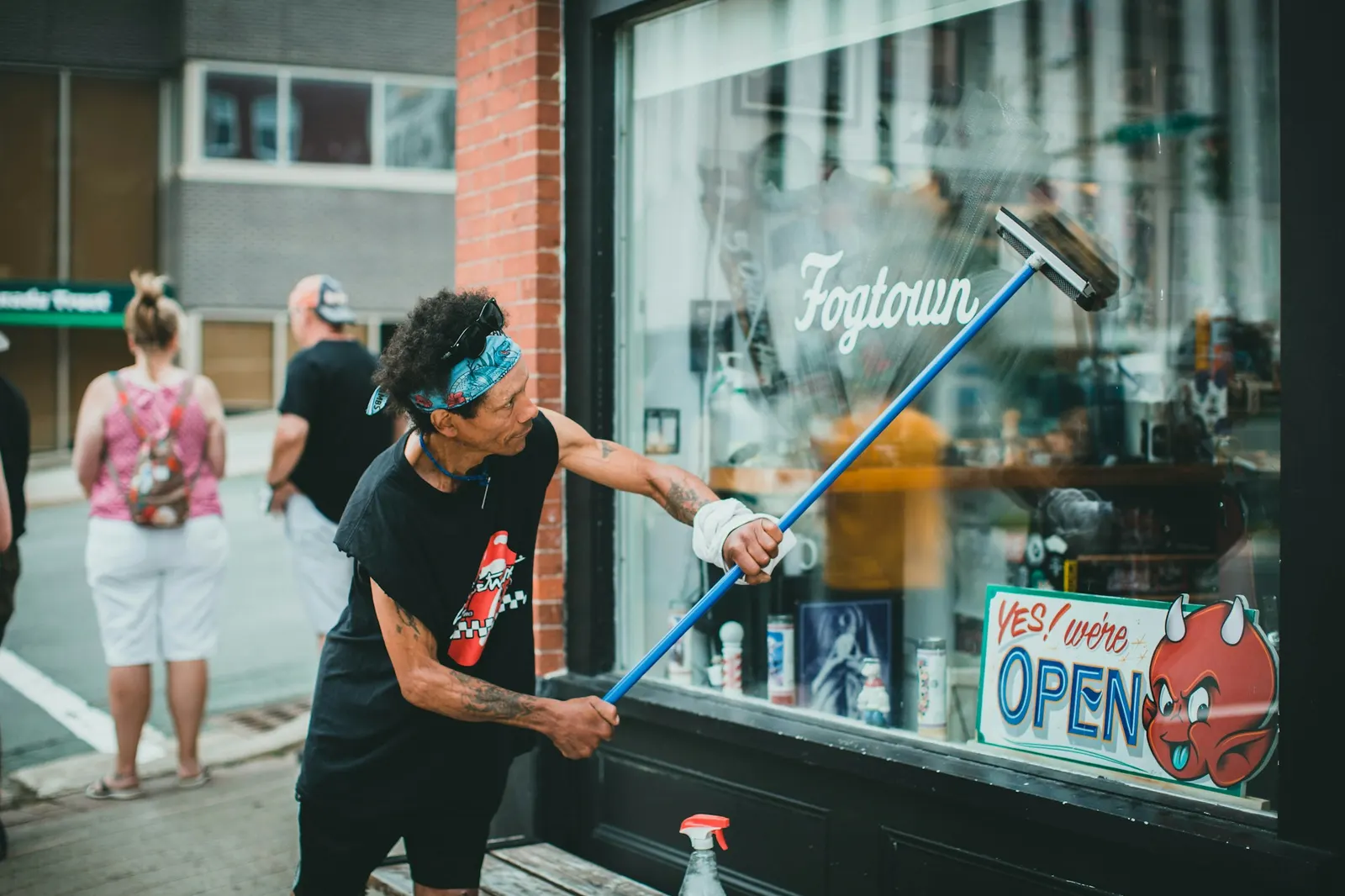 Window cleaner pulling a blue squeegee across a storefront window on a sunny street