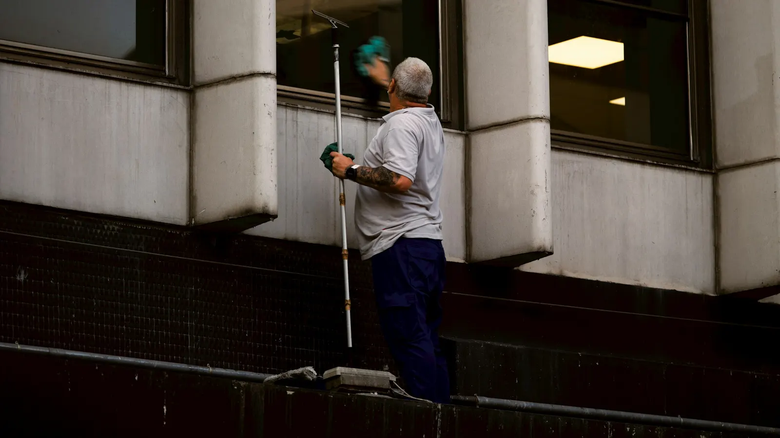 Window cleaner pulling a long squeegee across the glass exterior of a building