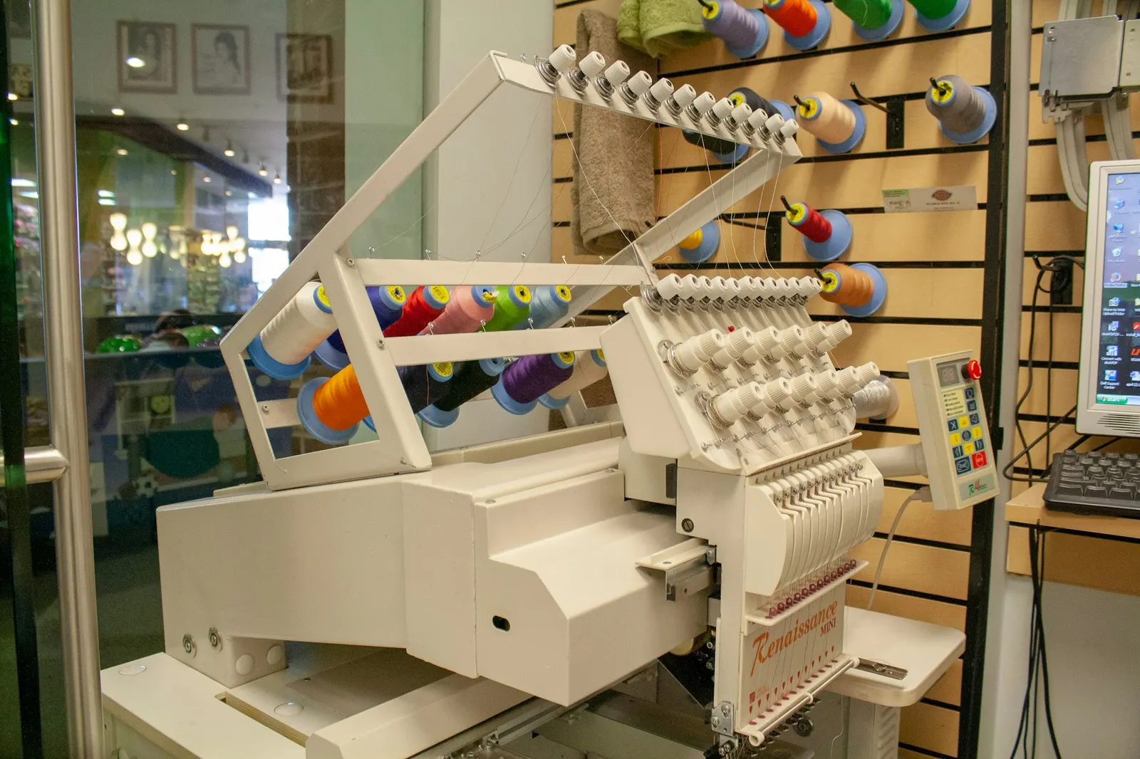 Multi-needle embroidery machine loaded with thread cones in a small shop